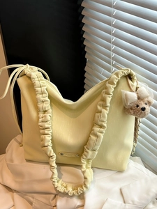 Minimalist pale yellow tote bag with pleated strap and brown plush bear charm