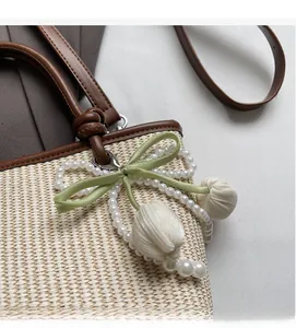 Close-up of pearl bead charms and green satin bow on a woven straw tote bag detail