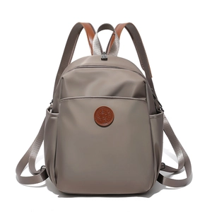 Close-up of taupe nylon backpack featuring brown leather handle and circular logo patch