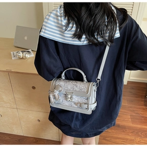 Detail of light gray vintage floral handbag with silver buckle and plush bear pendant
