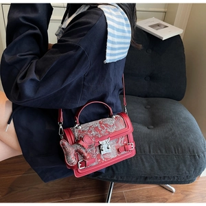 Detail of red square handbag with white floral patterns and matching bear bag charm