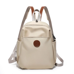 Detail of beige nylon backpack with brown leather logo patch and front zipper pocket