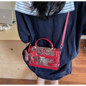 Detail of red crossbody bag with silver wave embroidery and metal twist lock on a model