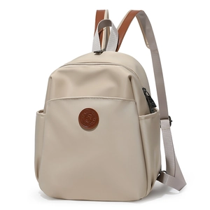 Close-up of beige nylon backpack with brown leather brand patch and zipper pocket