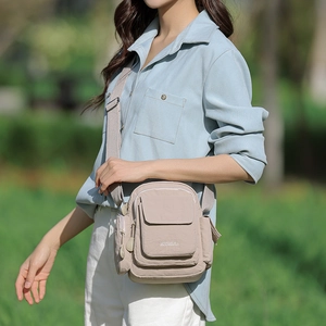 Outdoor shot of a beige nylon crossbody bag with multi-zipper layers and wide strap