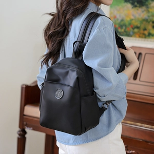 Black nylon mini backpack shown from a side view on a model in a warm indoor setting