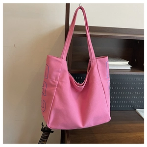 Detailed close-up of large pink canvas tote bag with blue letter print on wooden shelf