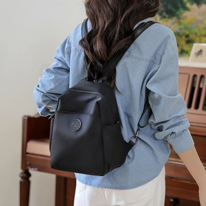 Rear view of a stylish black nylon backpack worn by a model in an elegant indoor setting
