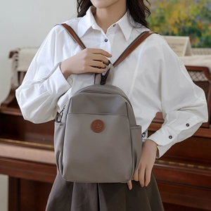 Detail view of neutral gray nylon backpack with brown leather logo badge and straps