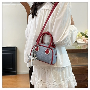 Dettaglio borsa a cuscino in denim blu con manici in pelle rossa e ciondolo stella