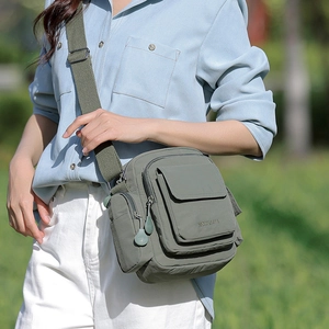 Detailed outdoor shot of an olive green nylon crossbody bag with multiple zip pockets