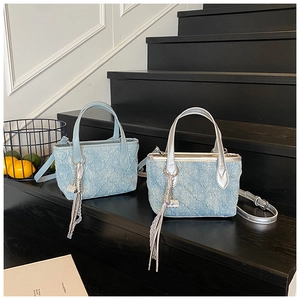 Detail of light blue denim mini tote bags with tassel charms and silver metal handles