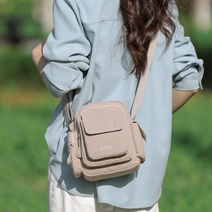 Detail of beige nylon crossbody bag with multi-pocket design and front flap pocket