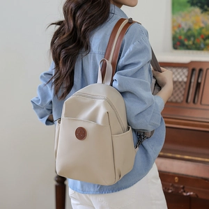 Detail of a cream nylon mini backpack with brown leather straps shown on a model