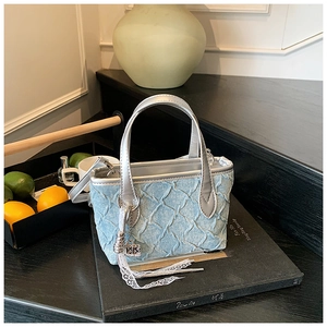 Close-up of light blue textured bucket bag with silver handles and lace tassel