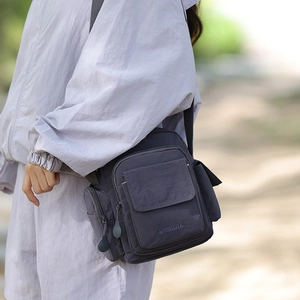 Detail of a dark purple-grey nylon crossbody bag with multiple zipper pockets on a model
