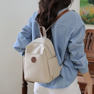 Rear view of a minimalist beige backpack showing straps and side pocket on a model