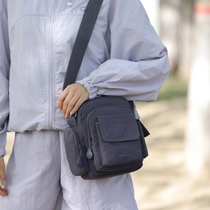 Outdoor shot of a grey nylon crossbody bag with adjustable wide strap and multi-pockets