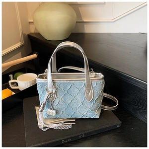 Detail of light blue denim texture handbag with silver metallic straps and lace fringe