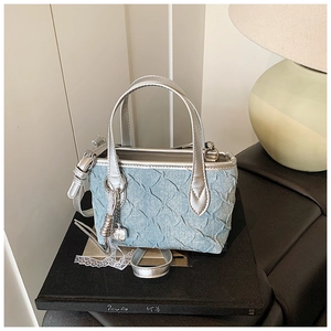Detail of light blue pleated denim handbag with silver handle and metallic lock charm