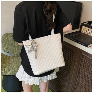 Detail of white woven texture tote bag featuring a decorative silver star charm on the side