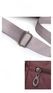 Detail of adjustable nylon strap and metal zipper on burgundy quilted crossbody bag