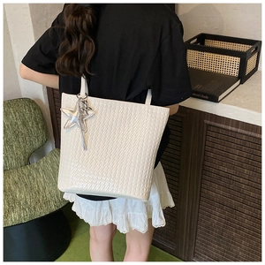 Detail of white woven bucket bag with silver star charm shown on shoulder for daily commute