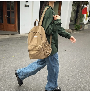 Outdoor street view of a large khaki canvas backpack with side pockets on a model