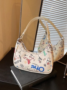White canvas hobo bag with colorful graffiti and adjustable strap on a book