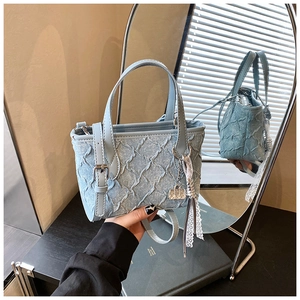 Detail of light blue denim bucket bag featuring quilted texture and lace tassel charm