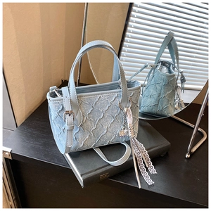 Detail of light blue denim bucket bag with pleated texture and white lace tassel charm
