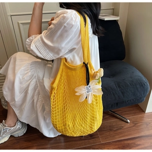 Detail of yellow knit tote bag featuring large mesh weave and white flower charm