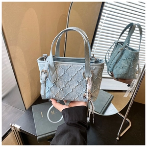 Detail of light blue pleated handbag with denim texture and metallic hardware accents