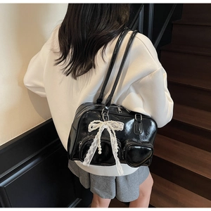 Detail of black patent leather hobo bag with white lace bow and pearl charm pendant