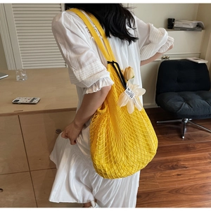 Detail of yellow knit mesh tote bag featuring a white tulip floral charm and texture