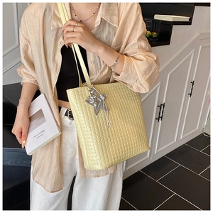 Detail of cream woven tote bag with silver star charm worn by a model in a minimal setting