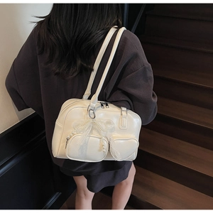 Close-up of cream shoulder bag with heart-shaped pockets and pearl bow charm