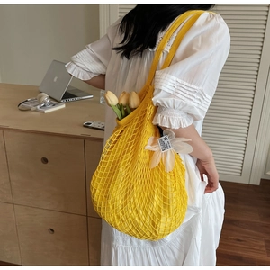 Detail of a large yellow knitted mesh tote bag featuring a white floral charm and inner pouch