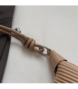Close-up of pleated leather texture and silver metal hardware on a brown handbag