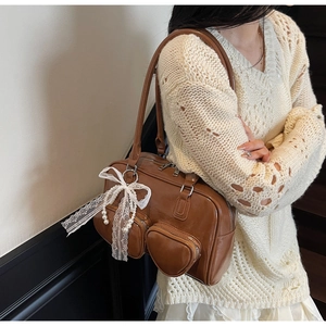 Detail of a brown patent leather handbag featuring heart-shaped pockets and lace bow with pearls