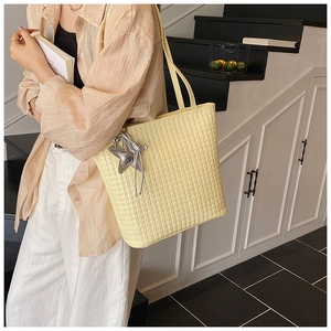 Detail view of yellow woven tote bag with silver star charm and mesh texture on shoulder