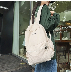 Outdoor shot of cream-colored nylon backpack featuring functional zipper pockets and side slots