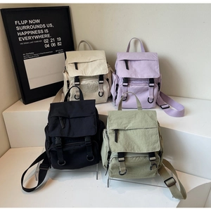 Detail view of mini canvas backpacks in beige, lavender, black, and sage green colors