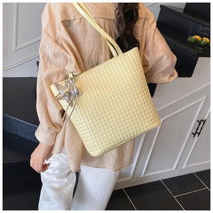 Detail of light yellow woven bucket bag featuring a shiny silver star charm and long strap