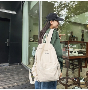 Street view of a cream large capacity canvas backpack with front zipper pocket detail