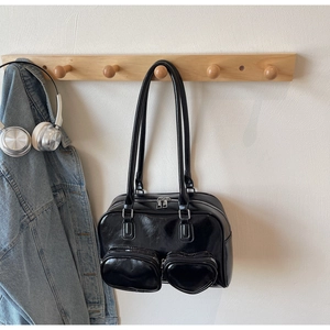 Detail of black glossy patent leather shoulder bag featuring a unique heart-shaped front pocket