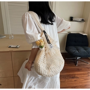 Detail of white mesh tote bag featuring a floral charm and black straps in home setting