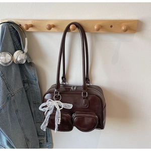Close-up of deep brown patent leather bag with lace bow and pearl charm on a hook