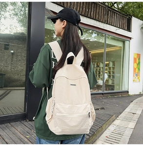 Outdoor back view of a person wearing a beige canvas backpack with adjustable straps
