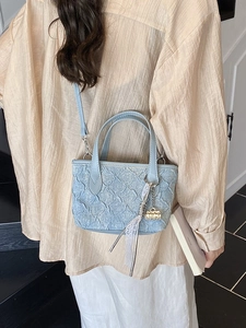 Light blue denim handbag with ruffled texture and lace ribbon charm on a model
